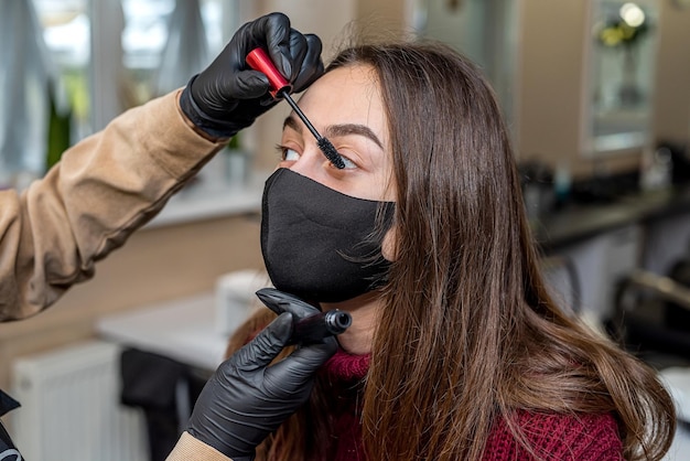 Une belle jeune cliente portant un masque noir spécial est venue au salon pour se maquiller pendant une pandémie