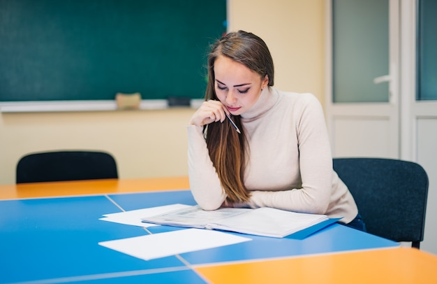 Belle jeune enseignante avec des notes est assise en classe