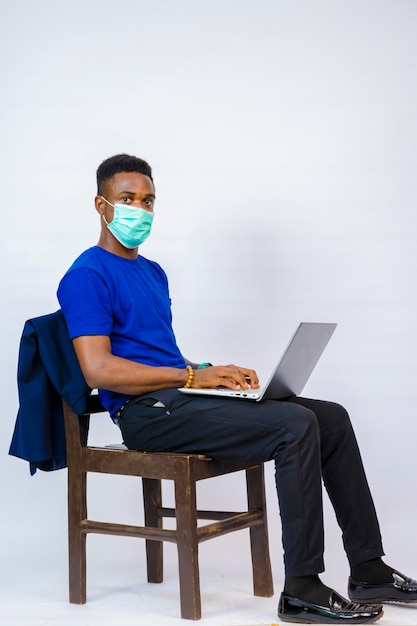 Une belle jeune entreprise africaine isolée sur fond blanc portant un masque facial pour se protéger de l'épidémie dans la société et se sent excitée et utilise son ordinateur portable