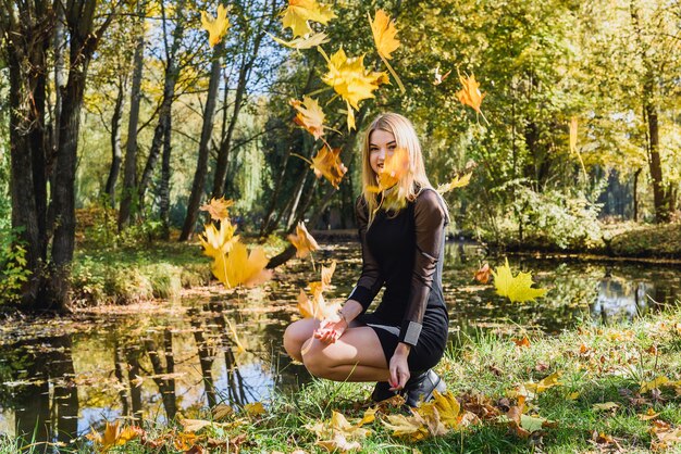 Belle jeune étudiante en robe noire tenant un bouquet de feuilles en automne parc.