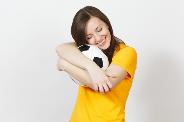 Belle jeune européenne joyeuse femme heureuse, fan de football ou joueur en uniforme jaune étreignant le ballon de football isolé sur fond blanc. Sport, jouer au football, santé, concept de mode de vie sain.