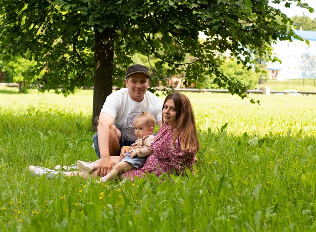 Belle jeune famille assise dans le parc sur l'herbe par une journée ensoleillée