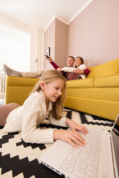 Belle jeune famille profitant d'une activité de loisir à la maison. Petite fille à l'aide d'un ordinateur portable, parent regardant une télévision. Mise au point sélective.