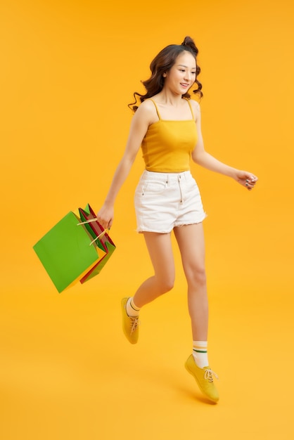 Belle jeune femme accro du shopping sautant en l'air avec des sacs à provisions sur fond orange.