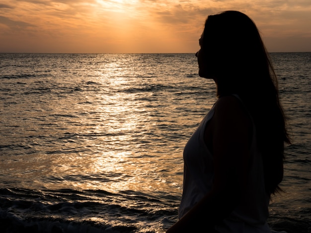 Belle jeune femme admirant le coucher de soleil sur la mer. Belle femme réunie avec la nature