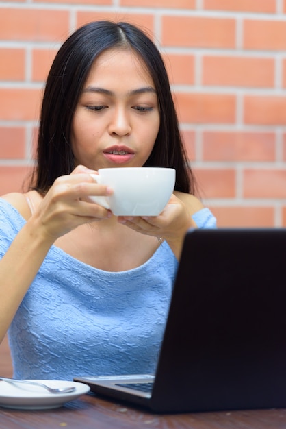 Belle jeune femme adolescente asiatique, boire du café avec un ordinateur portable sur une table en bois