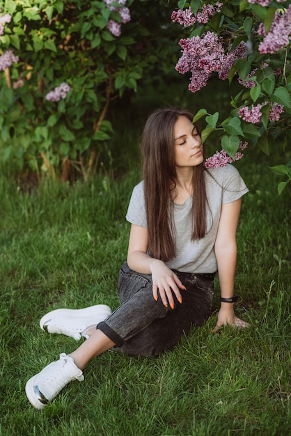 Belle jeune femme, adolescente, près d'un buisson de lilas dans un parc printanier ensoleillé. Mise au point sélective douce.