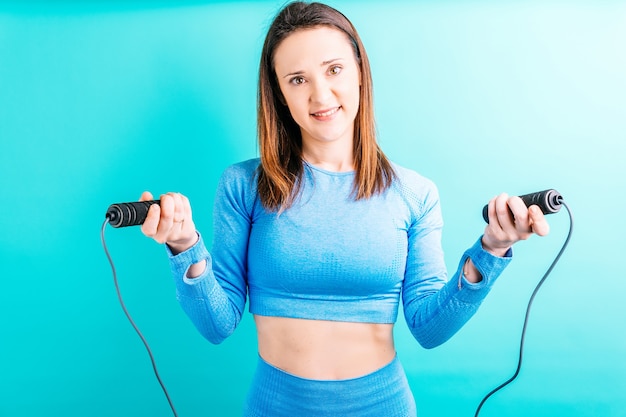 Belle jeune femme adulte en forme de collants de yoga regardant droit devant tenant une corde à sauter.concept de formation. sport avec espace de copie