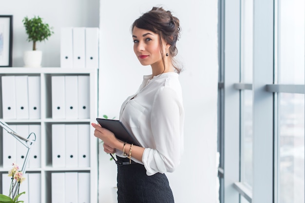 Belle jeune femme d'affaires à l'aide de tablette avec internet au bureau, la lecture et l'envoi de messages, souriant