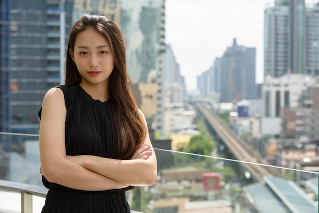 Belle jeune femme d'affaires asiatique avec les bras croisés contre vue sur la ville