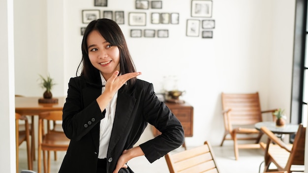 Belle jeune femme d'affaires asiatique en costume et pointant les mains vers le haut au bureau