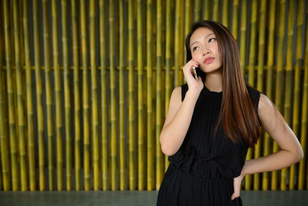 Belle jeune femme d'affaires asiatique parlant au téléphone contre une clôture en bambou