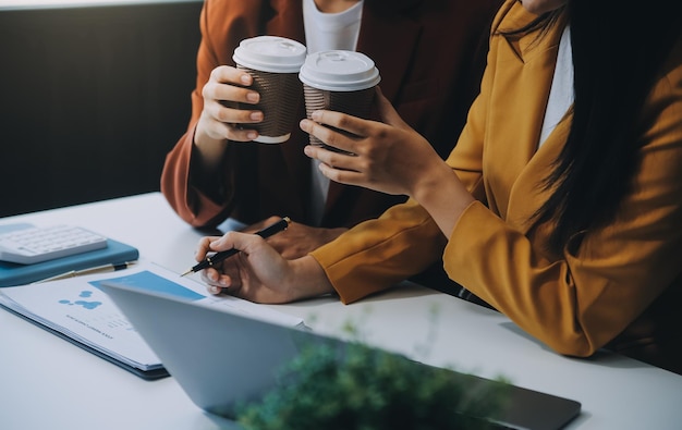 Une belle jeune femme d'affaires asiatique souriante travaillant sur un ordinateur portable et buvant du café Une femme d'affaire asiatique travaillant sur des documents financiers et une calculatrice dans son bureau