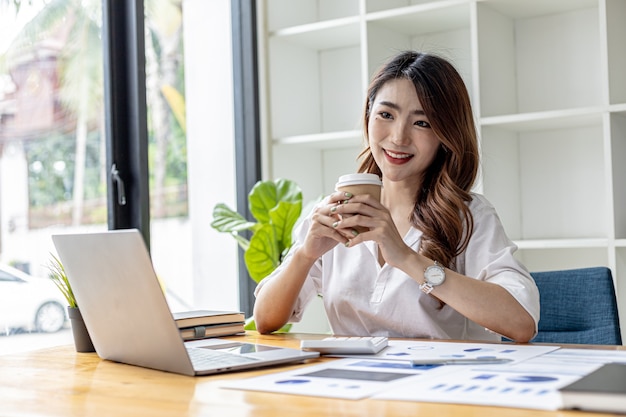 Belle jeune femme d'affaires buvant du café chaud. Une femme d'affaires boit du café pendant la journée, elle vérifie les documents du service financier. Concept de femme d'affaires asiatique.