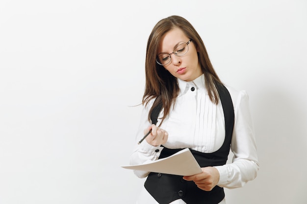 Belle jeune femme d'affaires caucasienne sérieuse en costume noir, chemise blanche, lunettes avec documents papier isolés sur mur blanc