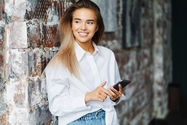 Belle jeune femme d'affaires en chemise blanche se tient près du mur de briques