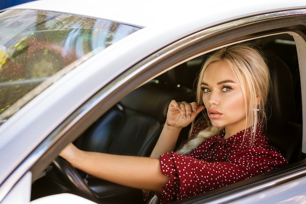 Belle jeune femme d'affaires dans une robe rouge assis dans une voiture