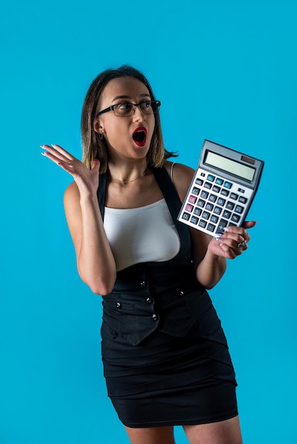 Belle jeune femme d'affaires dans des verres tenant une calculatrice isolée sur fond bleu