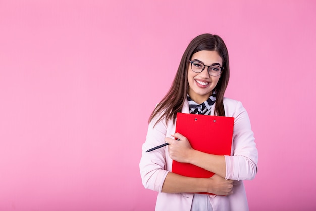 Belle jeune femme d'affaires écrit dans le presse-papiers isolé sur rose. Portrait souriant jeunes femmes d'affaires avec presse-papiers et document en mains