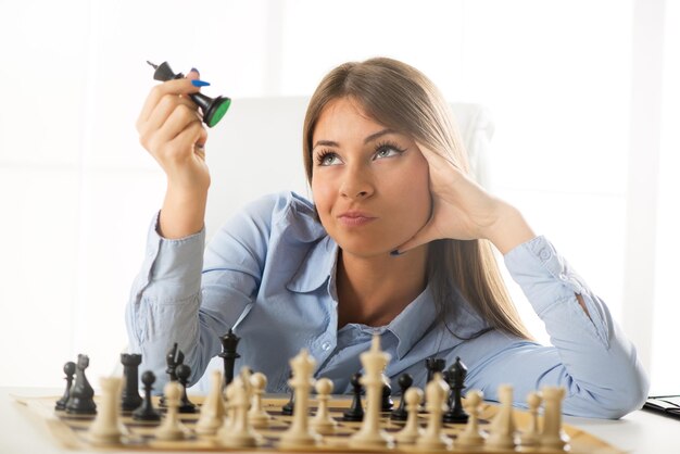 Belle jeune femme d'affaires élabore une stratégie d'entreprise. Elle est assise au-dessus de l'échiquier avec figure et réflexion.