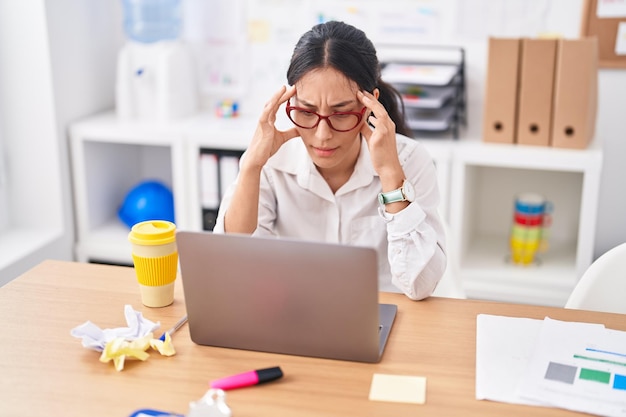 Belle jeune femme d'affaires hispanique stressée à l'aide d'un ordinateur portable au bureau