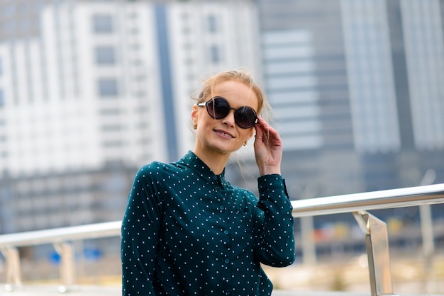 Belle jeune femme d'affaires avec lunettes de soleil, téléphone, ordinateur portable, tasse de café dans les rues de la ville.