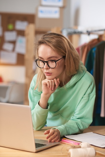 Belle jeune femme d'affaires à lunettes travaillant en ligne sur un ordinateur portable sur son lieu de travail