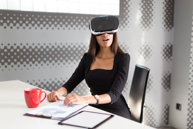 Belle jeune femme d'affaires en noir forte suite s'asseoir à la table de bureau dans des lunettes vr