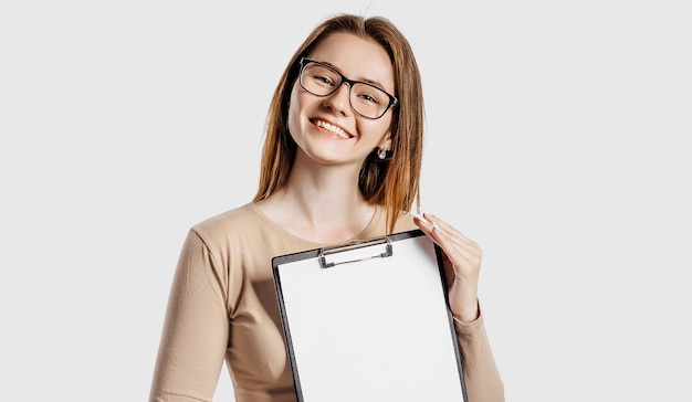 Belle jeune femme d'affaires portant des lunettes tient un presse-papiers avec maquette espace vide isolé sur un espace gris