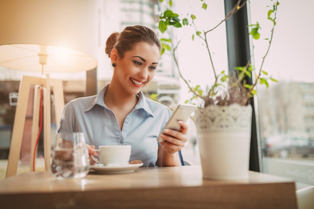 Belle jeune femme d'affaires souriante utilisant un téléphone intelligent dans un café.