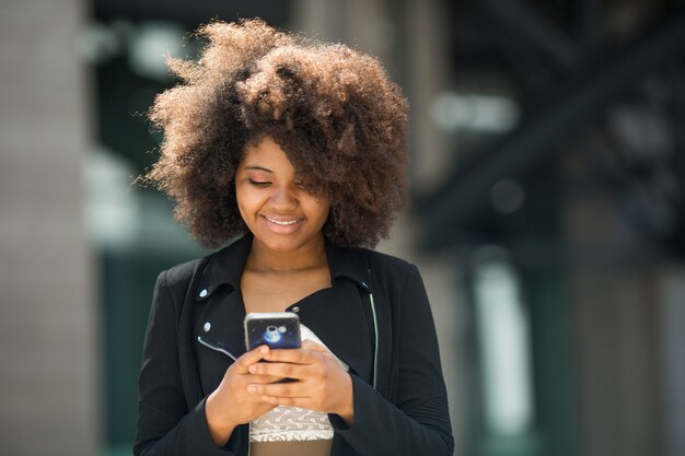 belle jeune femme africaine avec une coiffure volumineuse avec téléphone portable