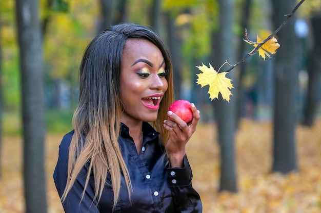 Belle jeune femme africaine mangeant une pomme rouge sur l'automne laisse de l'espace dans le parc