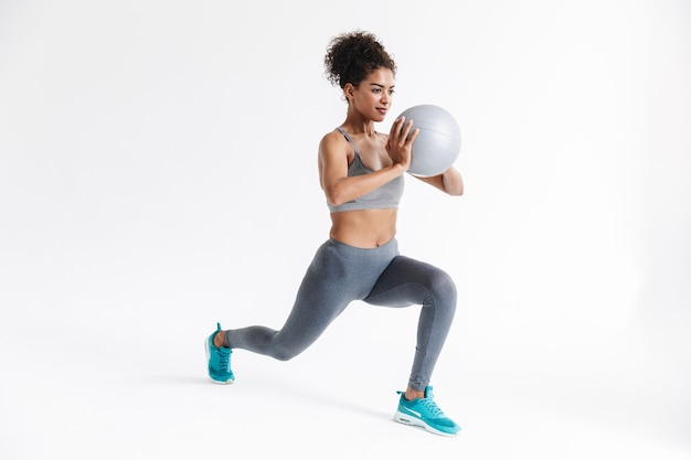 belle jeune femme africaine de remise en forme sportive incroyable posant isolée sur un mur blanc faire des exercices avec ballon.