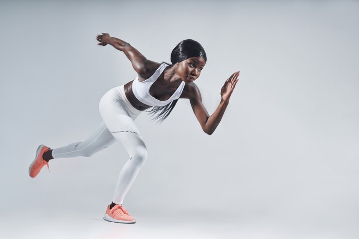 Photo belle jeune femme africaine en vêtements de sport en cours d'exécution sur fond gris