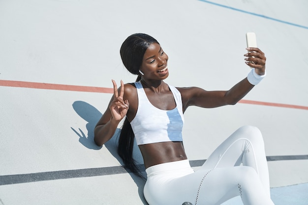 Belle jeune femme africaine en vêtements de sport faisant selfie et souriant