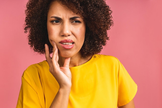 Belle jeune femme afro-américaine sur fond rose isolé touchant la bouche avec la main avec une expression douloureuse à cause d'un mal de dents ou d'une maladie dentaire sur les dents Concept de dentiste