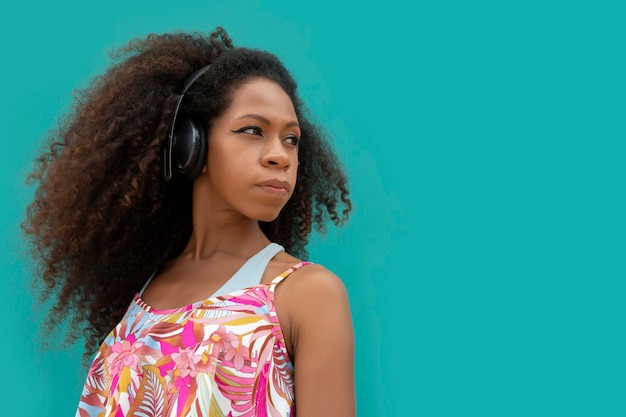 Belle jeune femme afro de profil avec un casque sur fond bleu aigue-marine