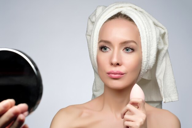 Belle jeune femme à l'aide d'une éponge de beauté pour appliquer le fond de teint pour le maquillage