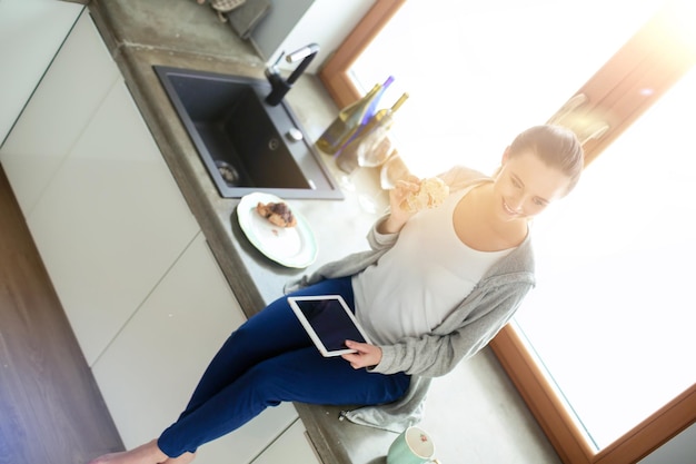 Belle jeune femme à l'aide d'une tablette numérique dans la cuisine