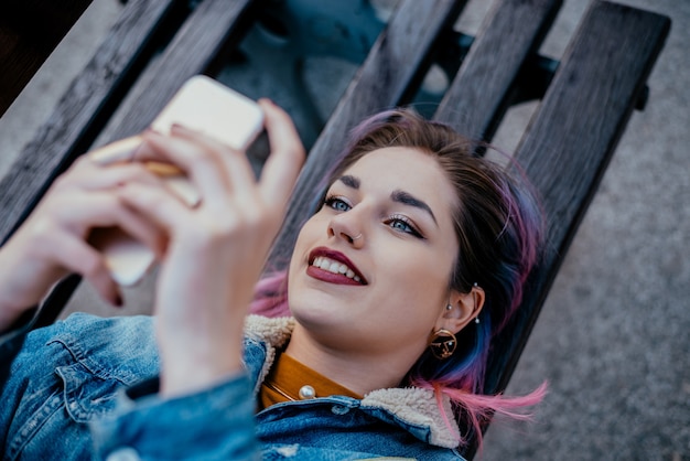 Belle jeune femme à l&#39;aide de téléphone en position couchée sur un banc.