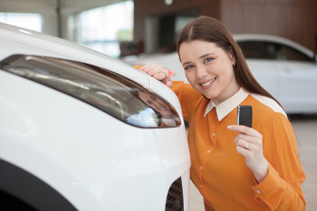 Belle jeune femme à l'air excitée, montrant la clé de sa nouvelle automobile chez le concessionnaire