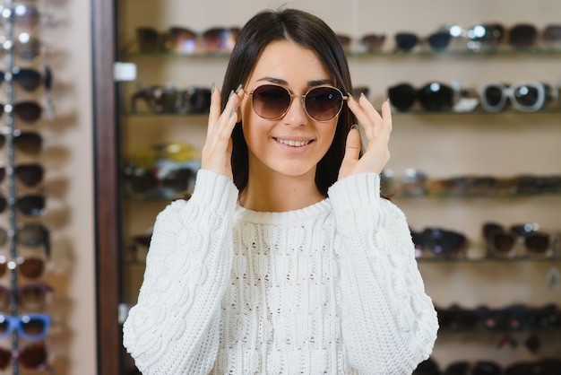 Belle jeune femme ajustant ses nouvelles lunettes de soleil debout dans le magasin d'optique