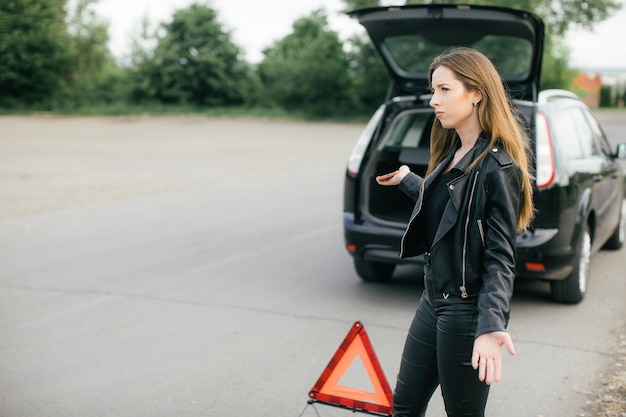 Belle jeune femme appelant à l'aide sur le bord de la route alors que sa voiture est cassée