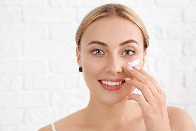 Belle jeune femme appliquant une crème pour le visage sur fond blanc