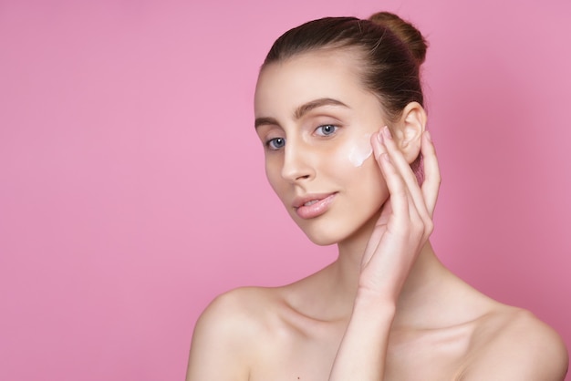 Belle jeune femme appliquant de la crème sur son visage rose