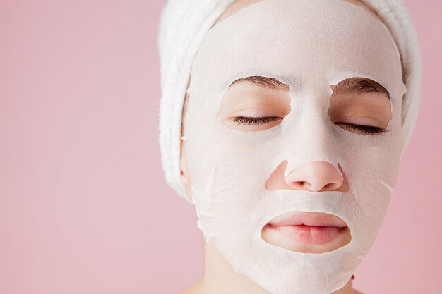 Belle jeune femme applique un masque de tissu cosmétique sur un visage sur une rose