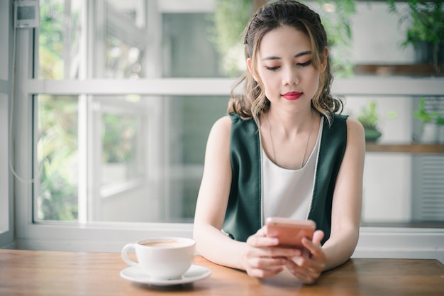 Belle jeune femme Asain touchant et parcourant son téléphone intelligent à la maison.