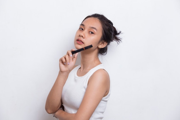 Belle jeune femme asiatique à l'aide de rouge à lèvres isolé sur fond blanc