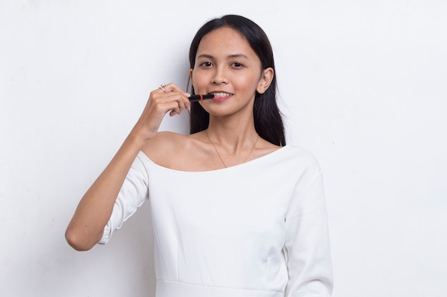 Belle jeune femme asiatique à l'aide de rouge à lèvres isolé sur fond blanc