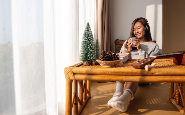 Une belle jeune femme asiatique aime boire du café et écouter de la musique avec un casque à la maison